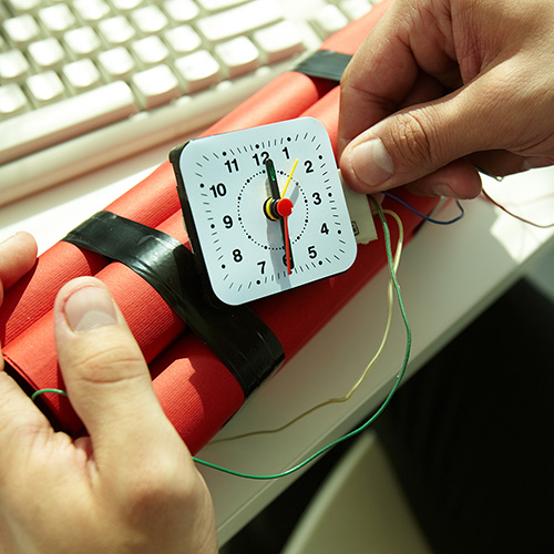 Hands holding dynamite explosive device near a computer keyboard