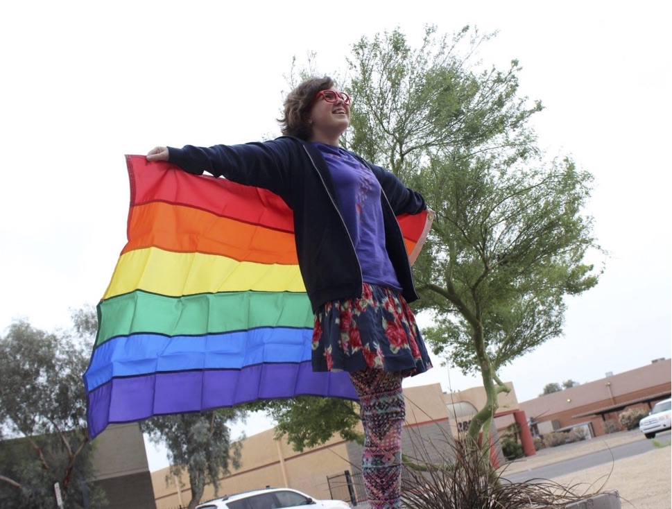 LGBTQ youth holding rainbow flag like a cape