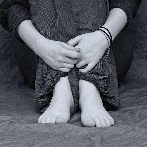 Cropped image of person seated, their hands holding their legs folded