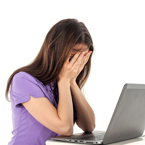 Girl sitting at computer with her hands over her face looking upset
